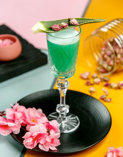 glas groene cocktail gegarneerd met aloë blad en gedroogde rozenknoppen