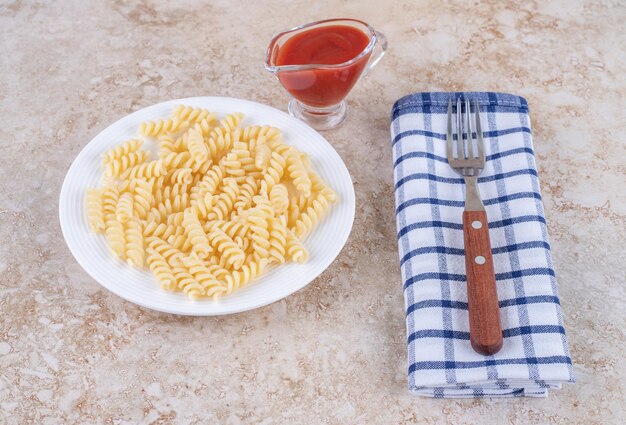 Glas ketchup, dressing voor dineropstelling met macaroni en vork op een handdoek op marmeren oppervlak