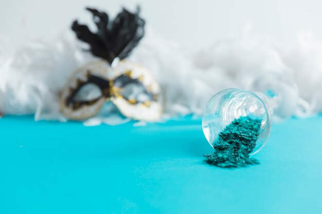 Glas met blauwe confetti in de buurt van masker