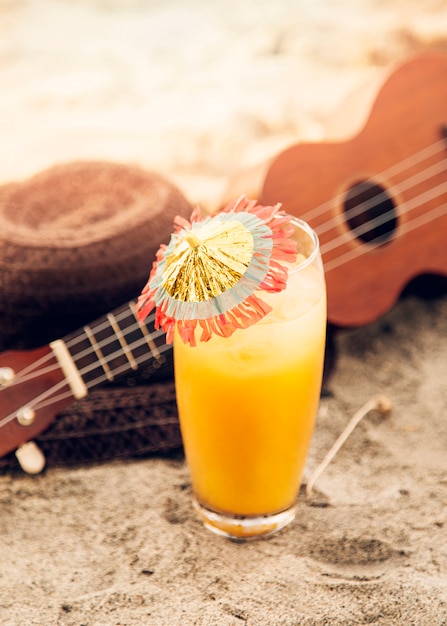 Gratis foto glas met drank, ukelele en strooien hoed op zand