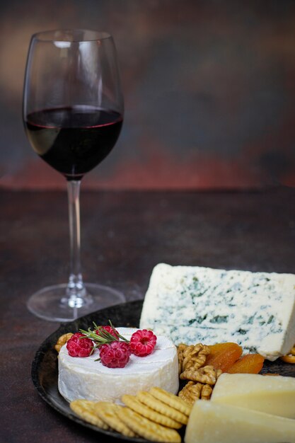 Glas rode wijn met kaasplaat op donker met camembertkaas, blauwe kaas, gauda en bessen en snacks