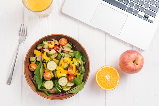 Glas sap; citrus sinaasappel; appel en gemengde groente salade met vork en laptop op witte houten bureau