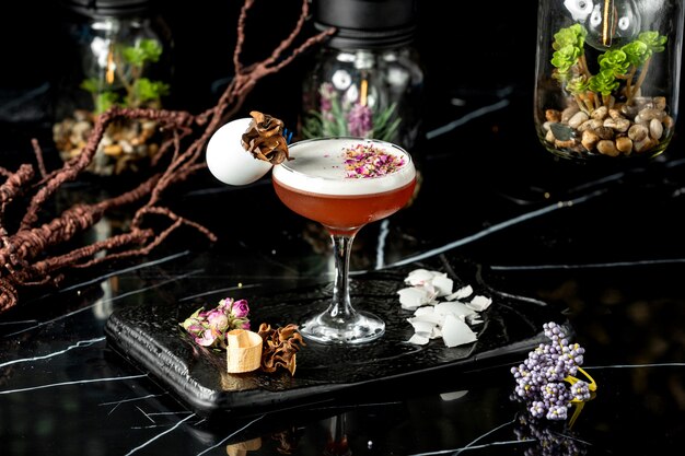 glas schuimende cocktail gegarneerd met stukjes gedroogde rozenblaadjes en eierschaal