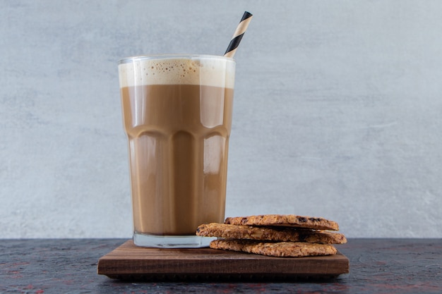 Glas schuimige koude koffie met koekjes op houten plaat.