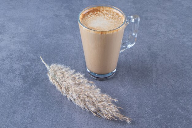 Glazen kopje koffie latte naast pampagras, op de blauwe tafel.