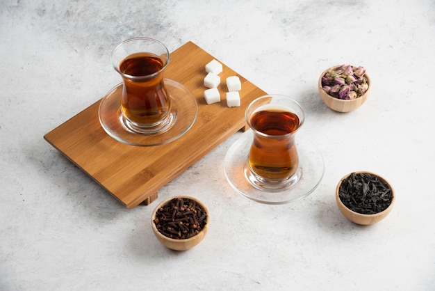 Glazen kopjes thee met suiker op een houten bord.