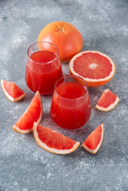 Glazen kopjes vers grapefruitsap met plakjes fruit op een houten bord.