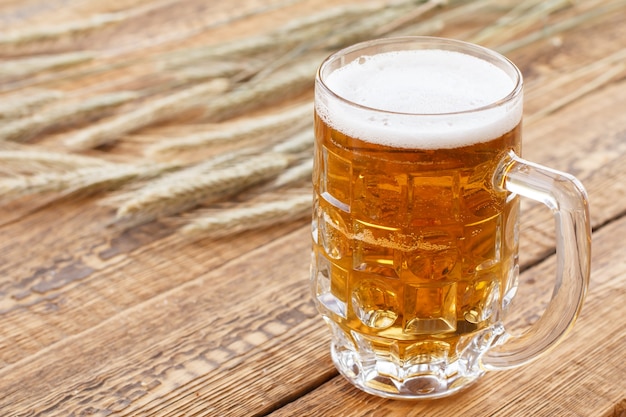 Glazen mok bier op oude houten planken met oren van gerst op een achtergrond.