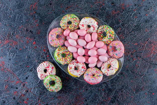 Glazen plaat van kleurrijke heerlijke donuts en roze snoepjes op donkere ondergrond.