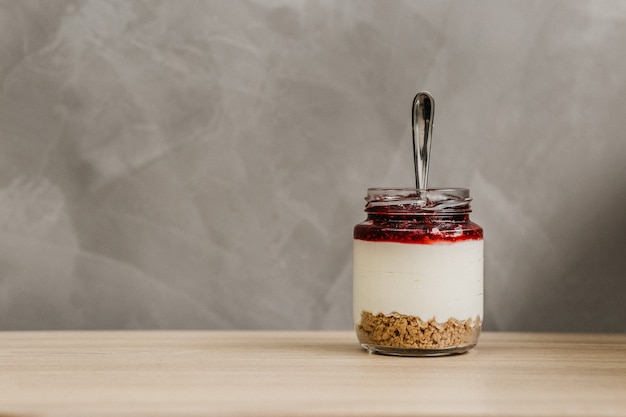 Glazen pot vol ontbijtgranen, yoghurt en fruitjam met een lepel erin