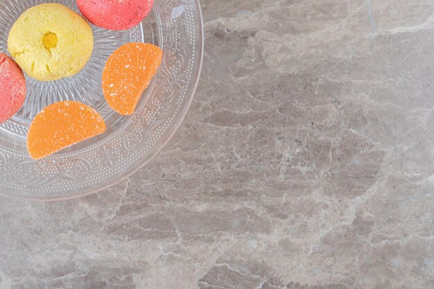 Glazen schaal met koekjes en gelei-snoepjes op marmeren oppervlak
