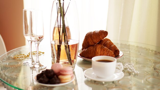 Glazen tafel met een kopje koffie, zoete croissants. op tafel staat een fles wijn en glazen. een feestelijke en romantische foto. ochtend na da