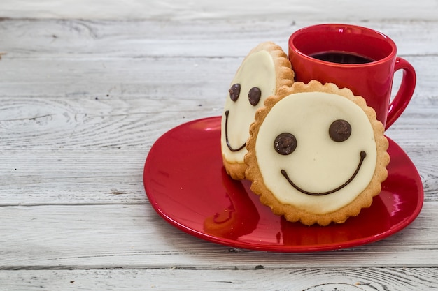 Glimlach koekjes op een rode plaat met kopje koffie, houten wand, eten