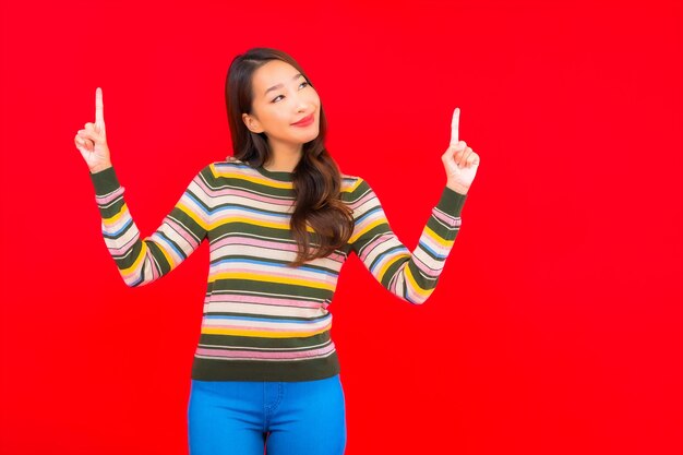 Glimlach van de portret de mooie jonge Aziatische vrouw met actie op rode geïsoleerde muur