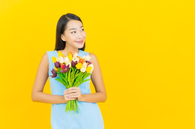 Glimlach van de portret de mooie jonge aziatische vrouw met bloem op gele kleurenmuur