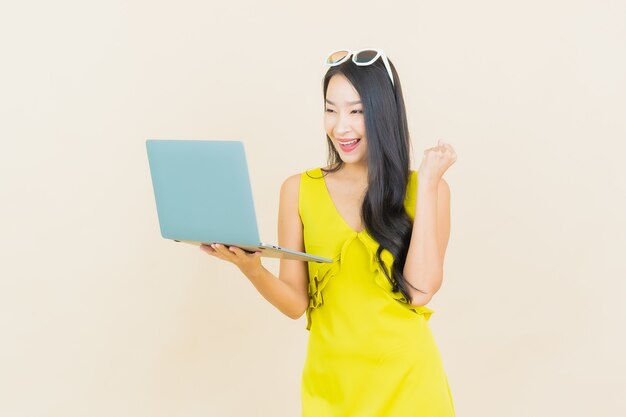 Glimlach van de portret de mooie jonge Aziatische vrouw met computerlaptop op geïsoleerde muur
