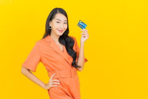 Glimlach van de portret de mooie jonge Aziatische vrouw met creditcard op geel