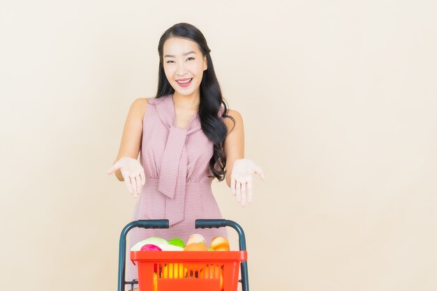 Glimlach van de portret de mooie jonge aziatische vrouw met kruidenierswinkelmandje van supermarkt