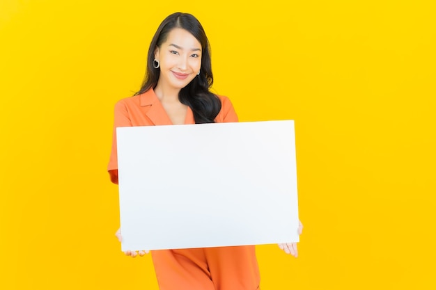 Glimlach van de portret de mooie jonge Aziatische vrouw met leeg wit aanplakbord op geel