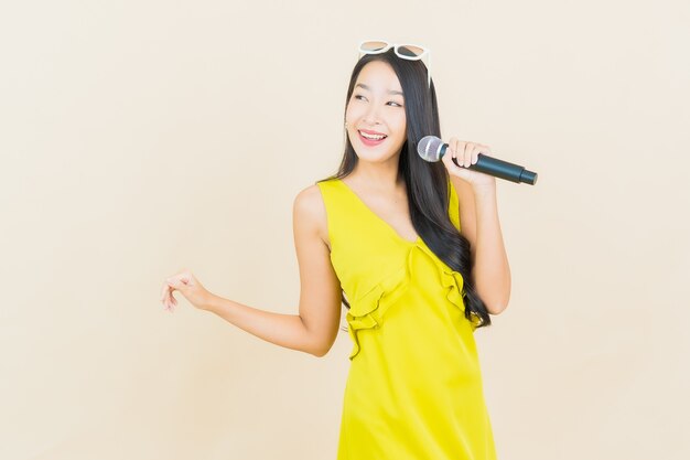 Glimlach van de portret de mooie jonge Aziatische vrouw met microfoon voor het zingen op muur