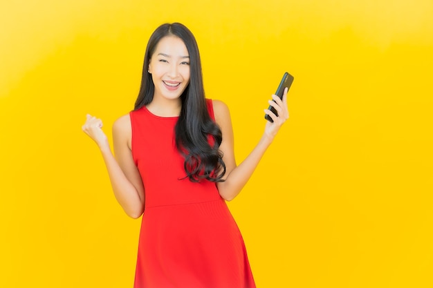 Glimlach van de portret de mooie jonge aziatische vrouw met slimme mobiele telefoon op gele muur