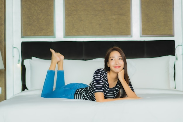 Glimlach van de portret ontspant de mooie jonge Aziatische vrouw op bed in slaapkamerbinnenland