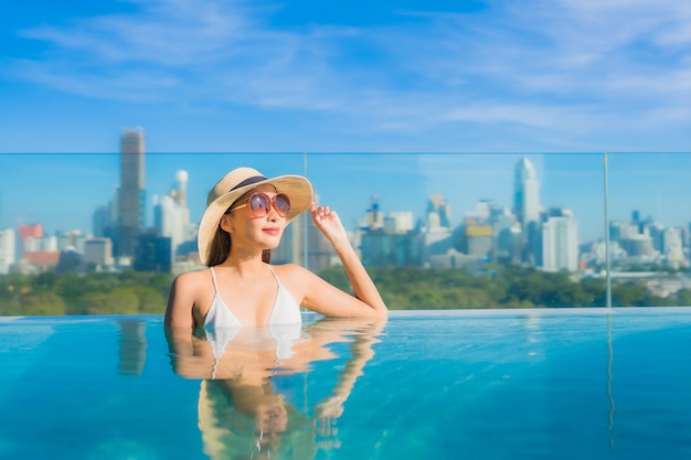 Glimlach van de portret ontspant de mooie jonge aziatische vrouw vrije tijd rond openluchtzwembad met stadsmening