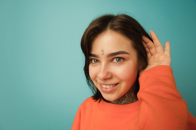 Glimlachen, close-up. Portret van de blanke vrouw geïsoleerd op blauwe muur met copyspace. Mooi vrouwelijk model in oranje hoodie. Concept van menselijke emoties, gezichtsuitdrukking
