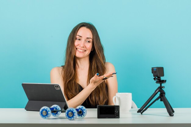 Glimlachend bloggermeisje poseert door met de hand naar rechts te wijzen op een blauwe achtergrond