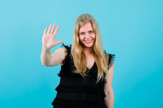 Glimlachend blond meisje toont haar handvol op blauwe achtergrond