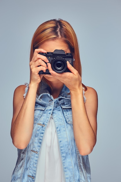 Glimlachend blonde vrouw houdt compacte digitale fotocamera, geïsoleerd op een grijze achtergrond.