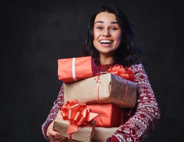 Glimlachend brunette vrouw in brillen en een warme trui houdt kerstcadeaus met felle kleureffect op de afbeelding.