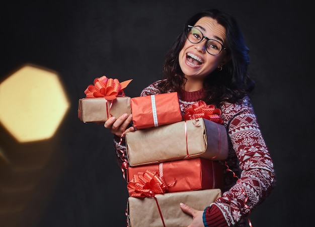 Glimlachend brunette vrouw in brillen en een warme trui houdt kerstcadeaus met felle kleureffect op de afbeelding.