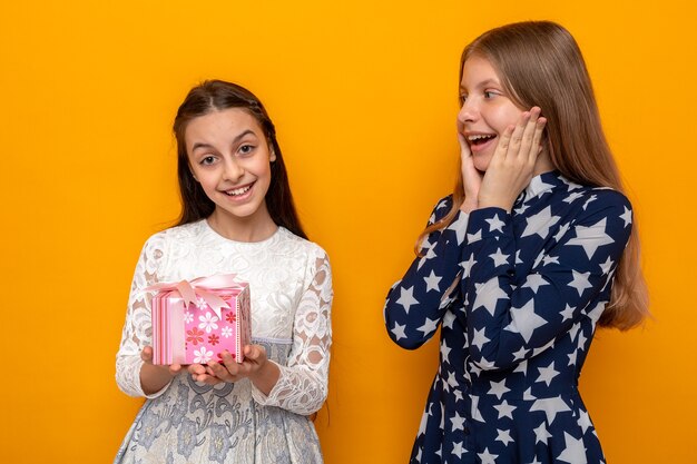 Glimlachend handen op de wangen zetten twee kleine meisjes die cadeautjes vasthouden