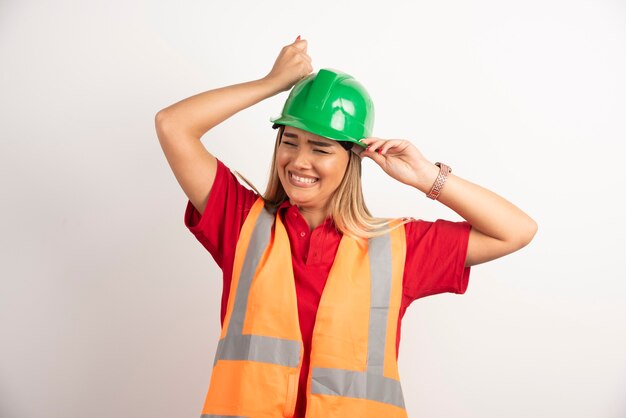 Glimlachend ingenieur vrouwelijke dragen uniform met harde groene helm op witte achtergrond.