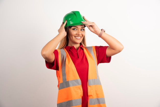 Glimlachend ingenieur vrouwelijke dragen uniform met harde groene helm op witte achtergrond.