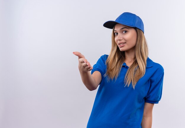 Glimlachend jong leveringsmeisje die blauw uniform en GLB dragen die hand standhouden die op witte muur met exemplaarruimte wordt geïsoleerd