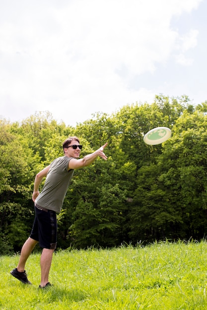 Glimlachend jong mannetje die plaat voor frisbee op weide werpen