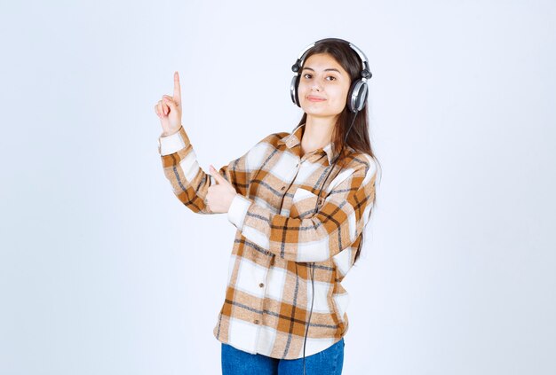 Glimlachend jong meisje in koptelefoon luisteren naar lied en wijzen.