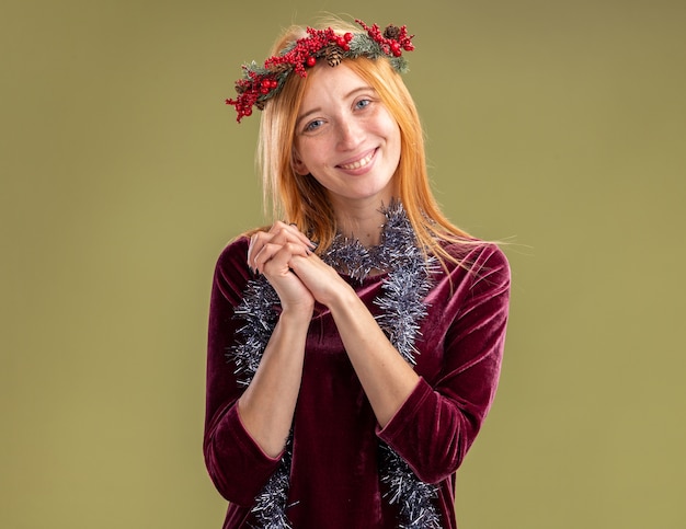 Gratis foto glimlachend jong mooi meisje dragen rode jurk met krans en garland op nek hand in hand samen geïsoleerd op olijfgroene achtergrond
