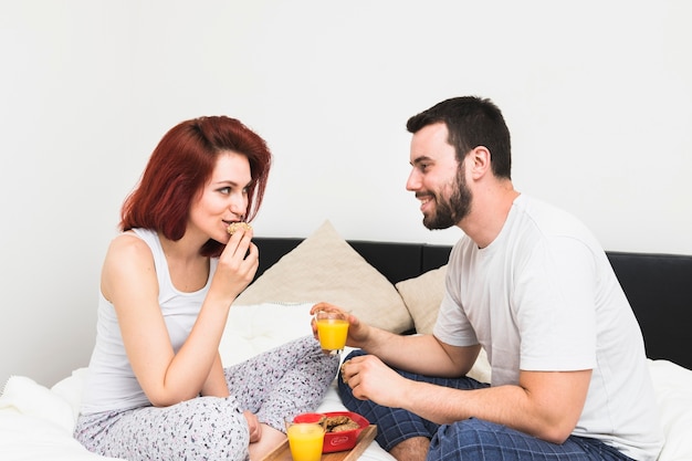 Gratis foto glimlachend jong paar dat ontbijt in slaapkamer heeft