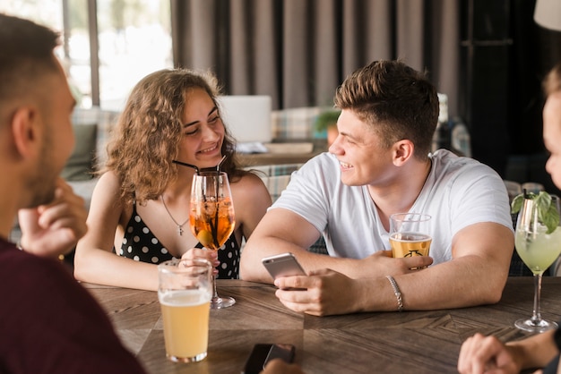 Glimlachend jong paar dat van dranken met vrienden in restaurant geniet