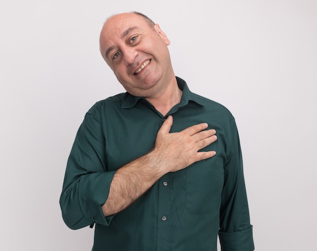 Glimlachend kantelend hoofd man van middelbare leeftijd met groene t-shirt hand op hart zetten geïsoleerd op een witte muur