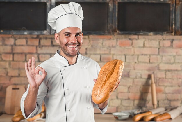 Glimlachend mannelijk de holdingsbroodje die van de bakker het ok gebaar van het handteken tonen