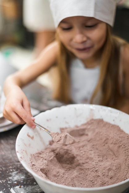 Glimlachend meisje dat een lepel van cacaopoeder van kom neemt