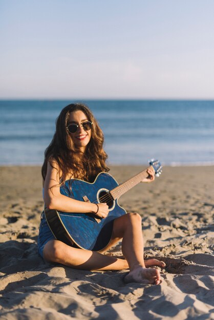 Glimlachend meisje dat gitaarzitting op het zand speelt