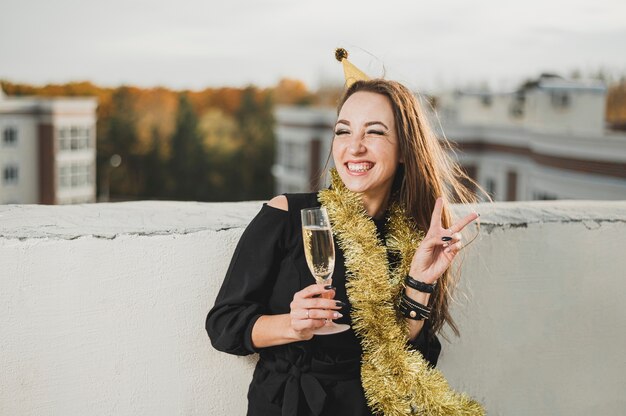 Glimlachend meisje dat in zwarte kleding een champagneglas houdt bij de partij op het dak