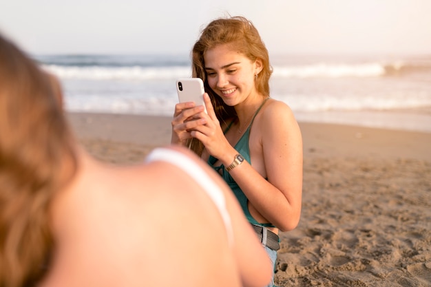 Glimlachend meisje die zelfportret van haar vriend nemen bij strand