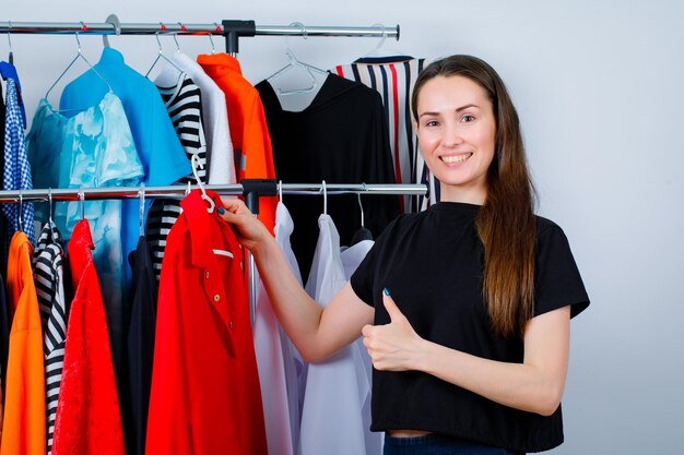 Glimlachend meisje houdt blouse vast en toont perfect gebaar op kledingachtergrond