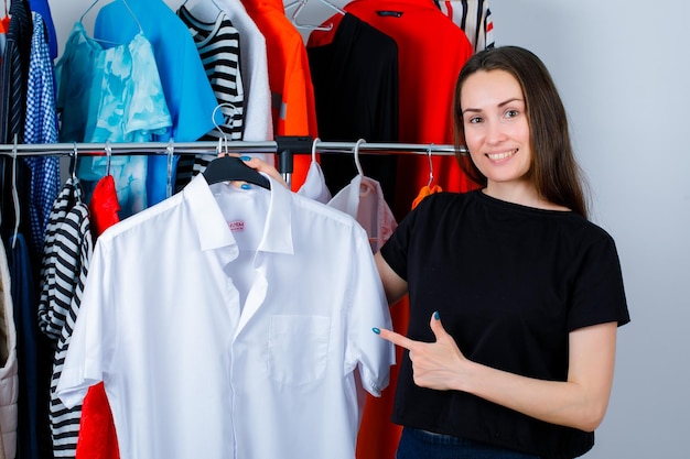 Glimlachend meisje houdt shirt vast en toont het met wijsvinger op kledingachtergrond